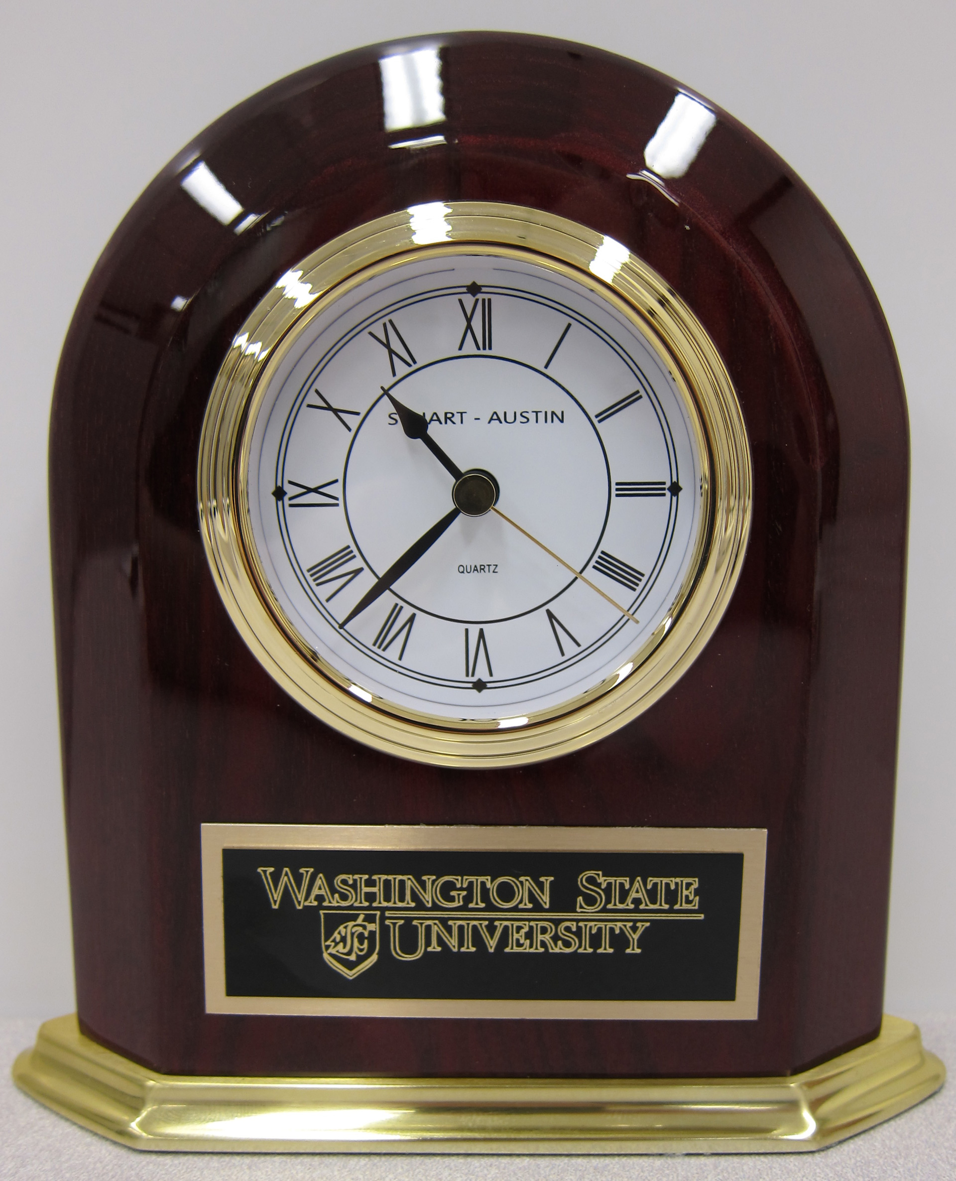 This rosewood finished table clock has a polished brass tone base and bezel and features a gold tone dial with black Roman numerals. 